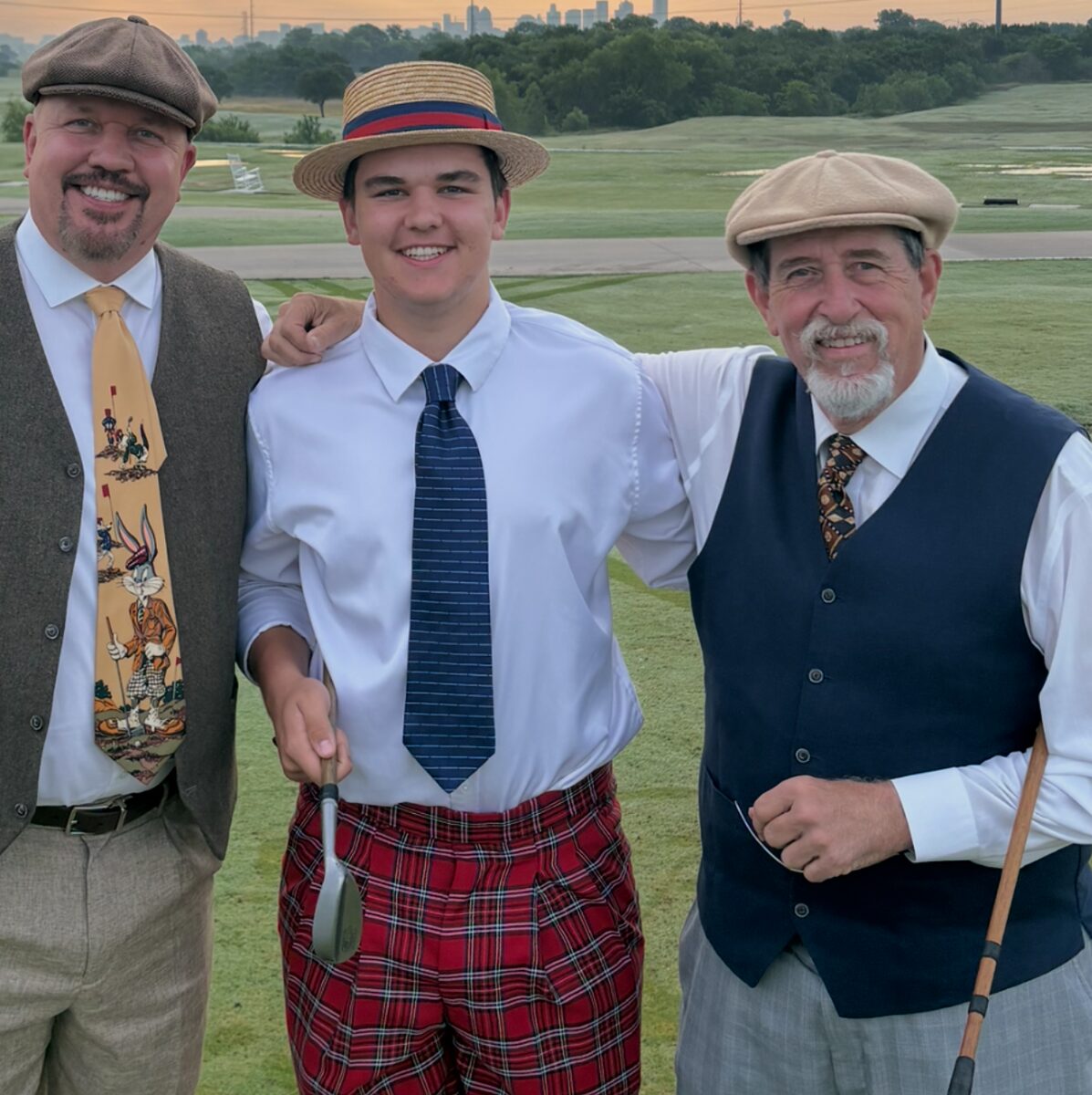 Three players in flat caps, a straw boater, vests, and plaid knickers at sunrise, with the city skyline behind the course
