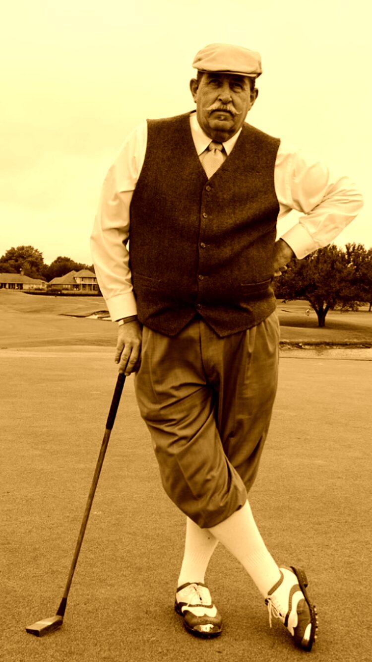 Ken Jackson in period golf attire &mdash; flat cap, tie, vest, and knickers &mdash; leaning on a hickory-shafted club on the course